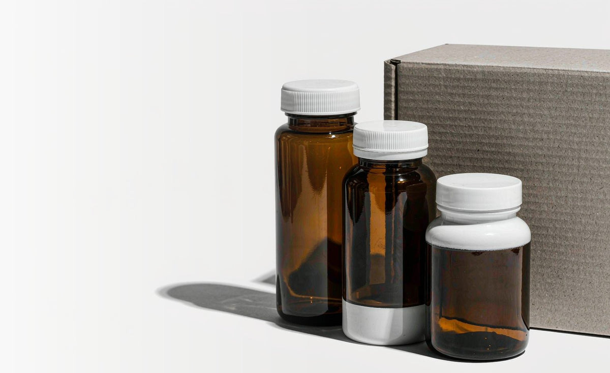 Set of unbranded supplement bottles beside a shipping box on a white background
